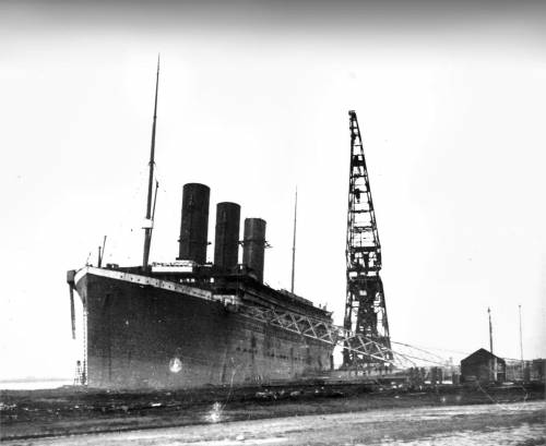 Данная фотография SS Titanic была сделана в декабре 1911 года. На снимке мы видим большой плавучий 200 тонный кран, два специальных решетчатых трапа, по которым поднимались рабочие для работ внутри лайнера. На самом лайнере уже установлены три дымовые трубы.